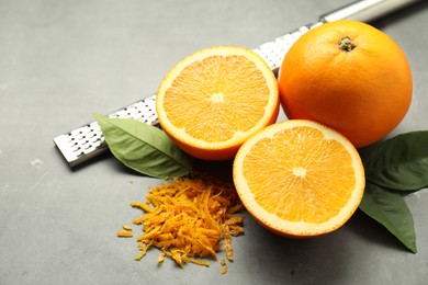 Photo of Pile of fresh orange zest, fruits, grater and leaves on grey table, closeup