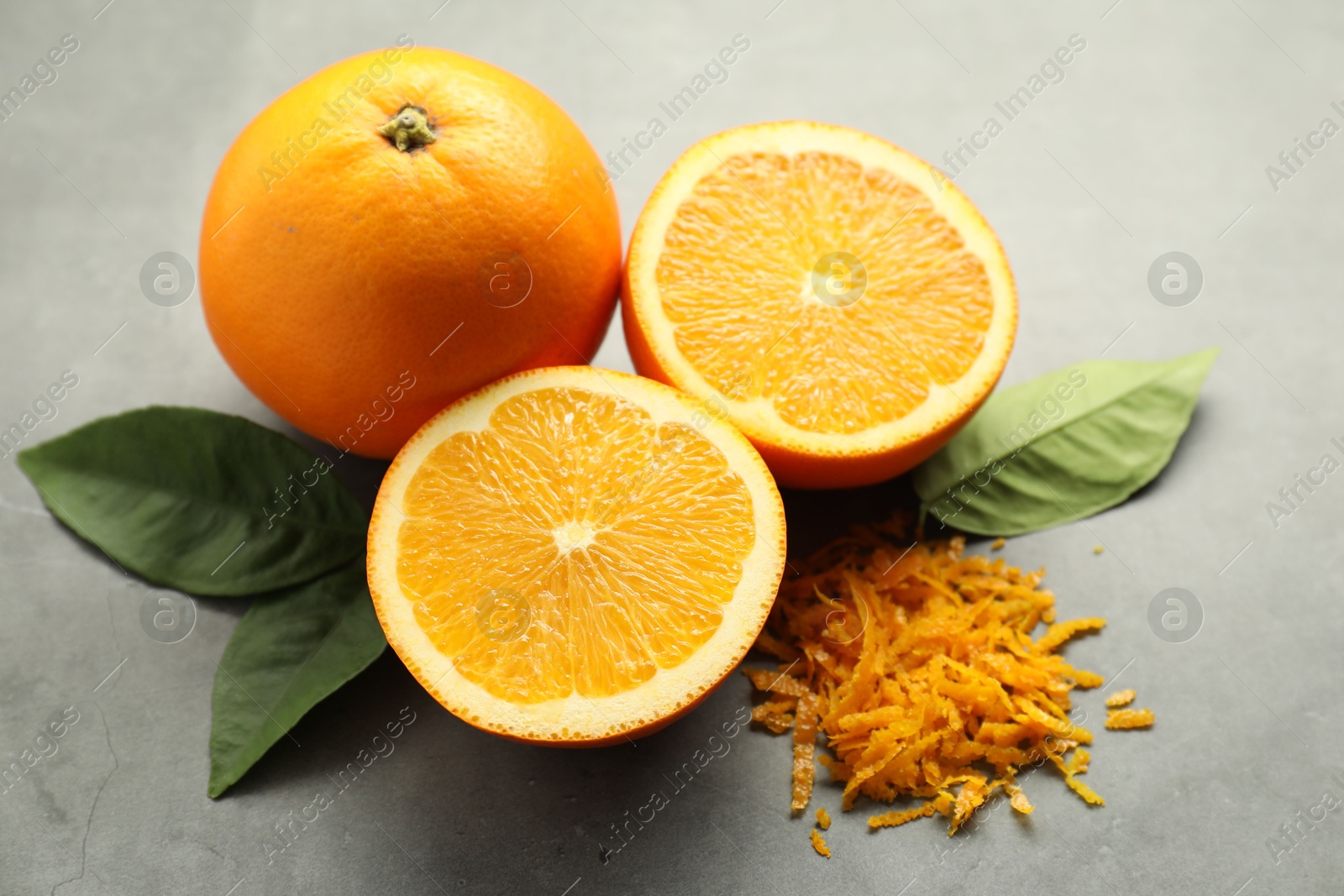 Photo of Pile of fresh orange zest, fruits and leaves on grey table