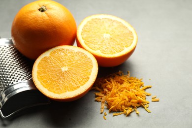 Photo of Pile of fresh orange zest, fruits and grater on grey table, closeup