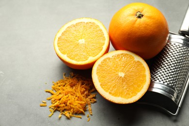 Photo of Pile of fresh orange zest, fruits and grater on grey table