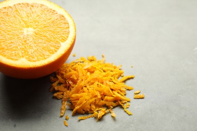 Photo of Pile of fresh orange zest and cut fruit on grey table, closeup. Space for text