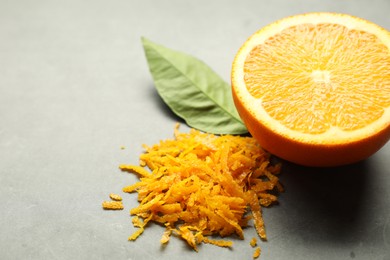 Photo of Pile of fresh orange zest, cut fruit and leaf on grey table, closeup. Space for text