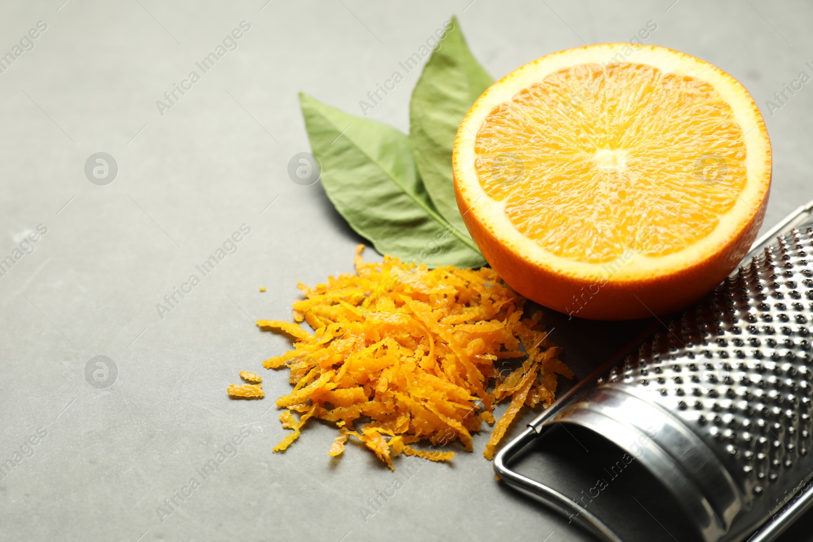 Photo of Pile of fresh orange zest, cut fruit, leaves and grater on grey table, closeup. Space for text