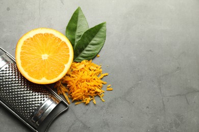 Photo of Pile of fresh orange zest, cut fruit, leaves and grater on grey textured table, flat lay. Space for text