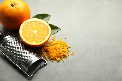 Photo of Pile of fresh orange zest, fruits, leaves and grater on grey table. Space for text