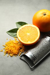 Photo of Pile of fresh orange zest, fruits, leaves and grater on grey table