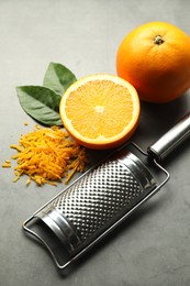 Photo of Pile of fresh orange zest, fruits, leaves and grater on grey table