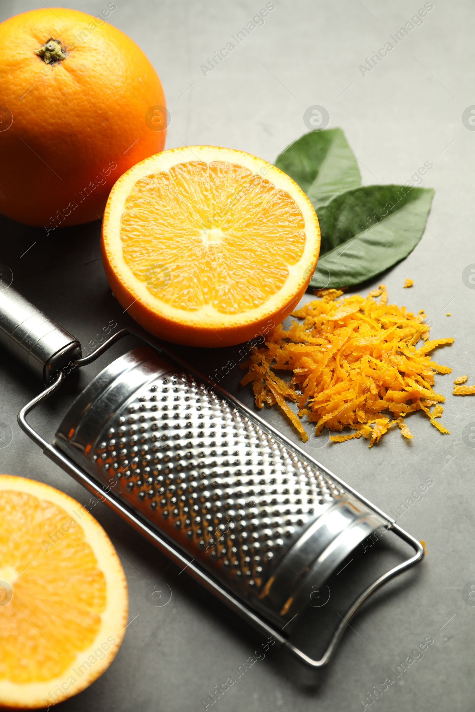 Photo of Pile of fresh orange zest, fruits, leaves and grater on grey table