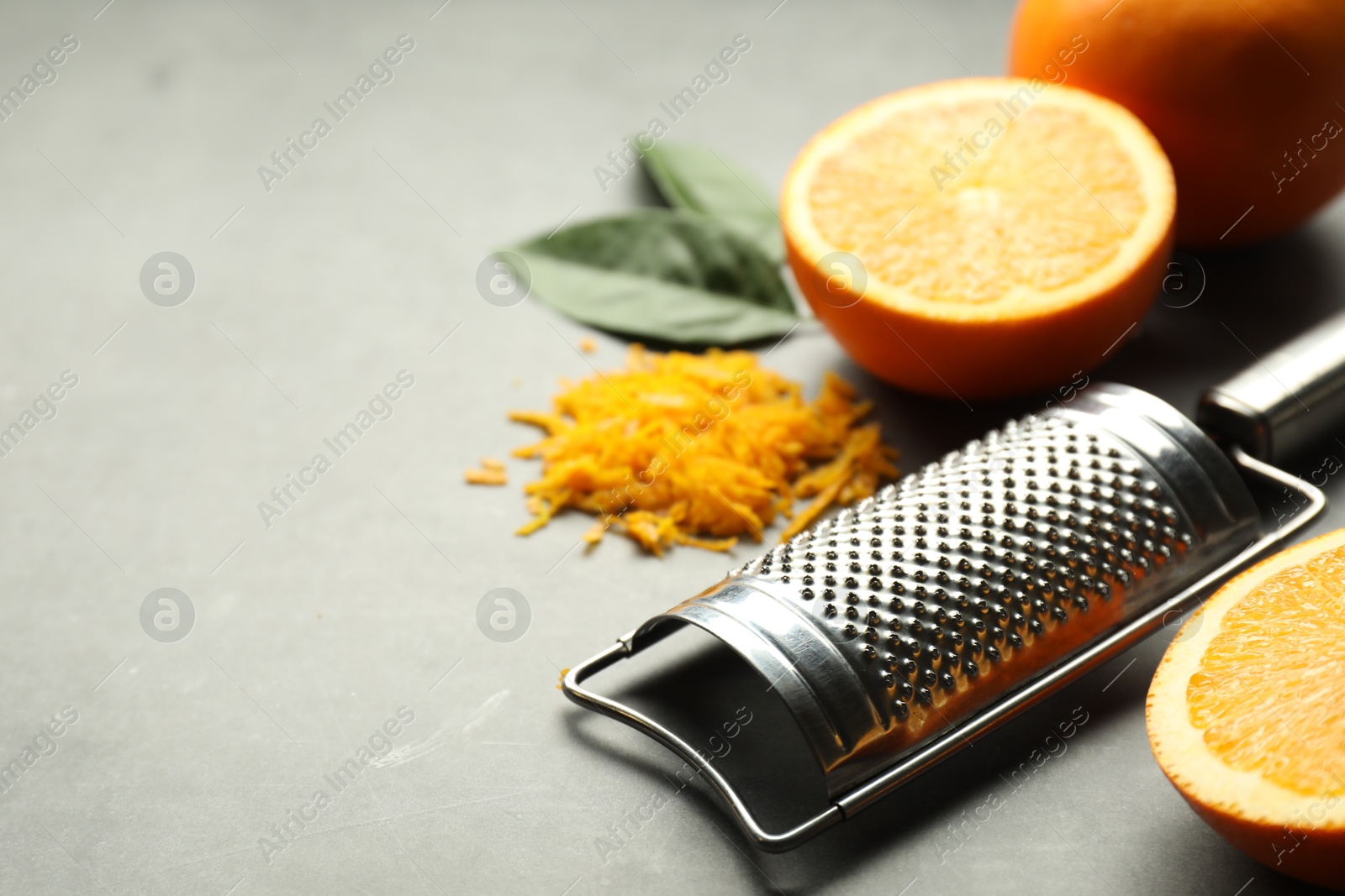 Photo of Pile of fresh orange zest, fruits, leaves and grater on grey table, closeup. Space for text