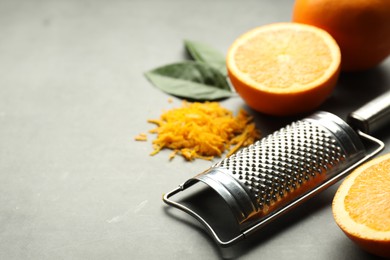 Photo of Pile of fresh orange zest, fruits, leaves and grater on grey table, closeup. Space for text