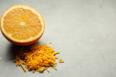 Photo of Pile of fresh orange zest and cut fruit on grey table, closeup. Space for text