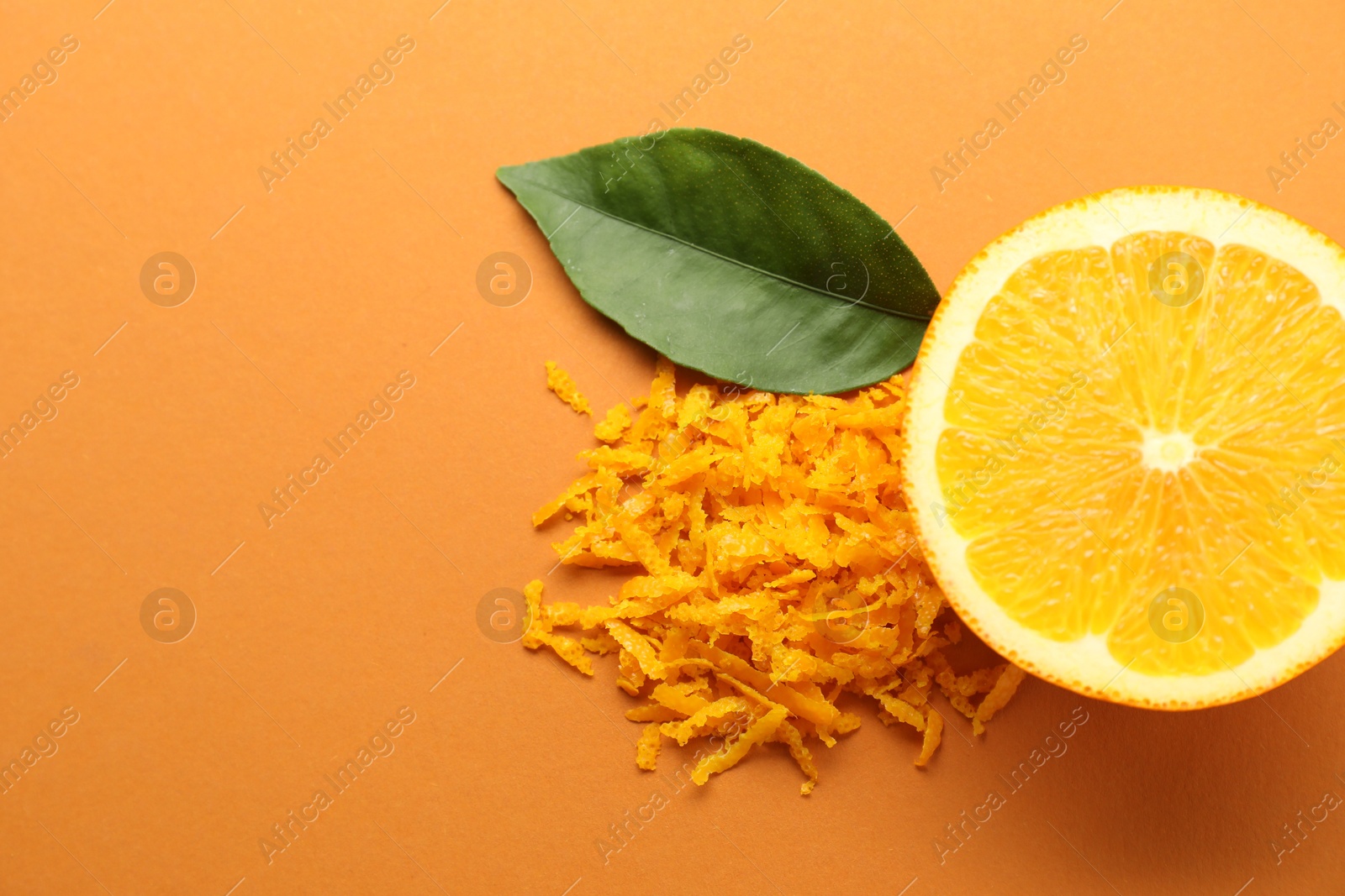 Photo of Pile of fresh orange zest, cut fruit and leaf on color background, flat lay. Space for text