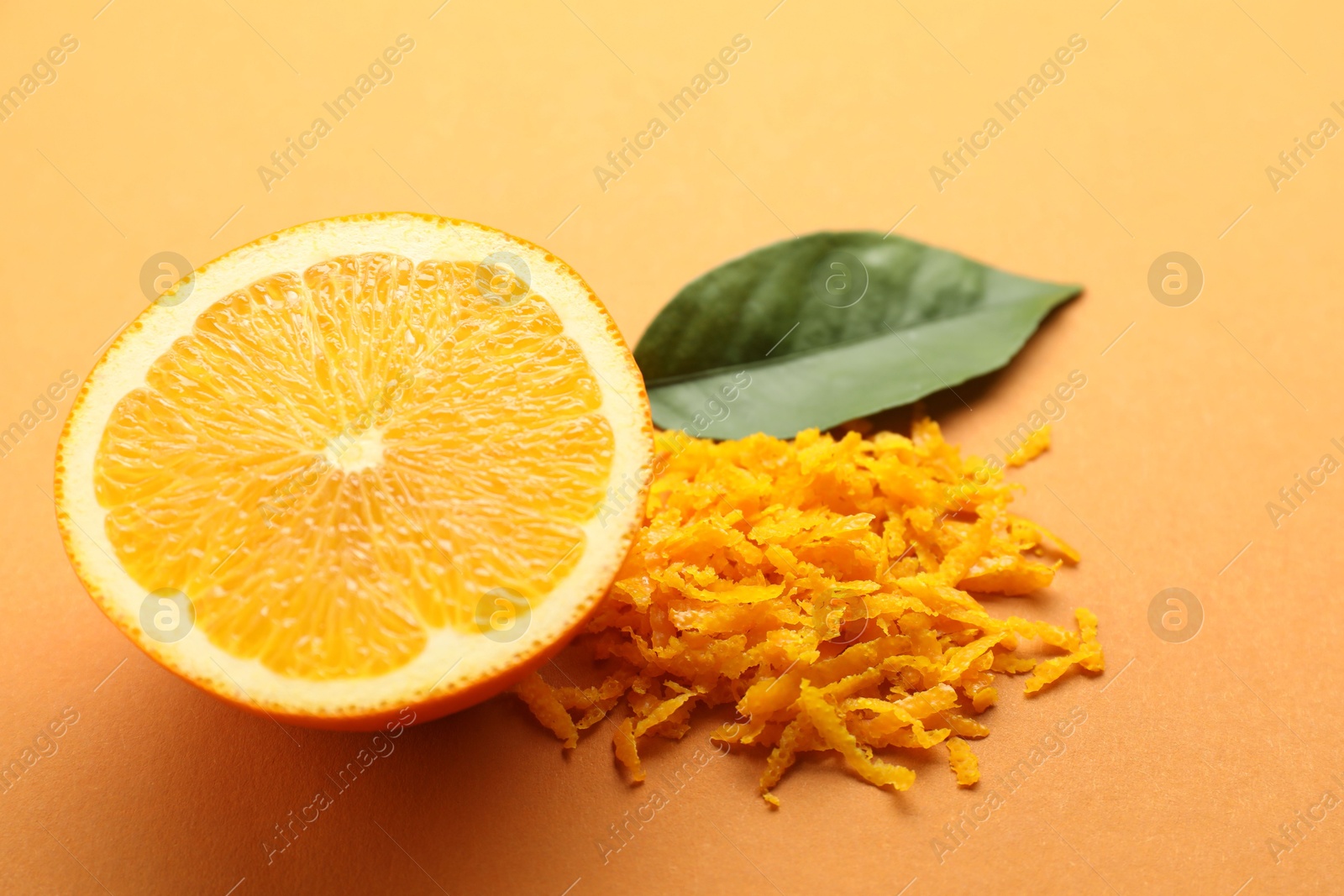 Photo of Pile of fresh orange zest, cut fruit and leaf on color background, closeup