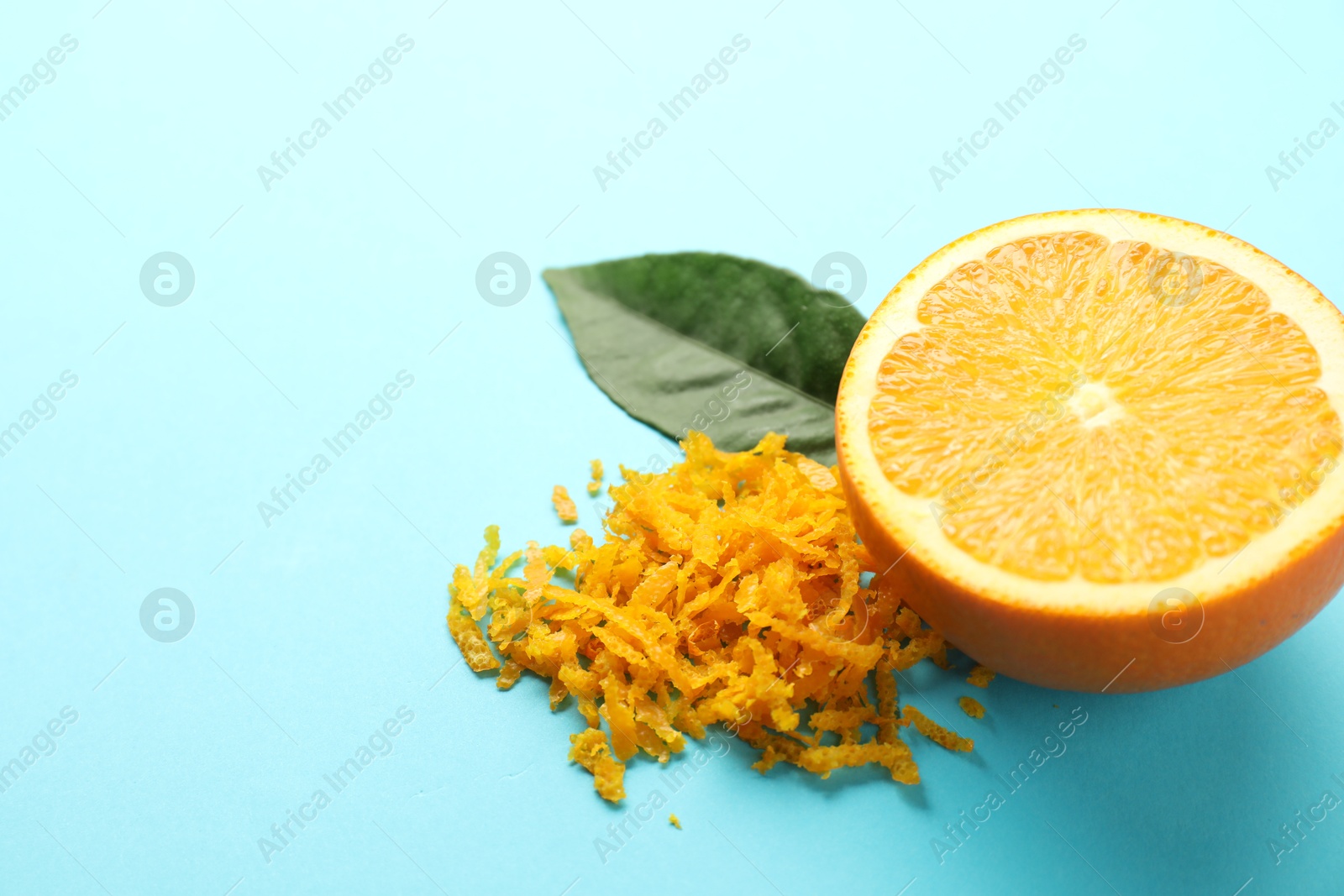 Photo of Pile of fresh orange zest, cut fruit and leaf on light blue background, closeup. Space for text