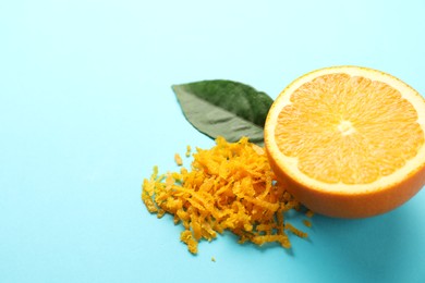 Photo of Pile of fresh orange zest, cut fruit and leaf on light blue background, closeup. Space for text