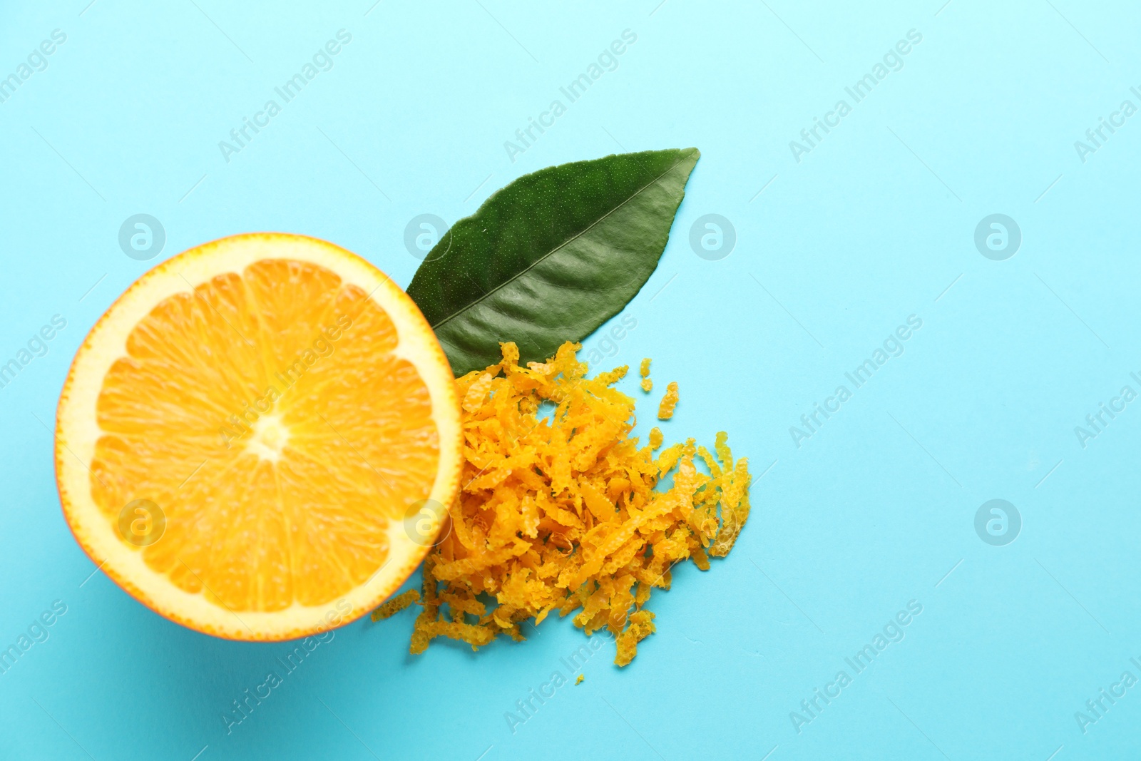 Photo of Pile of fresh orange zest, cut fruit and leaf on light blue background, flat lay. Space for text