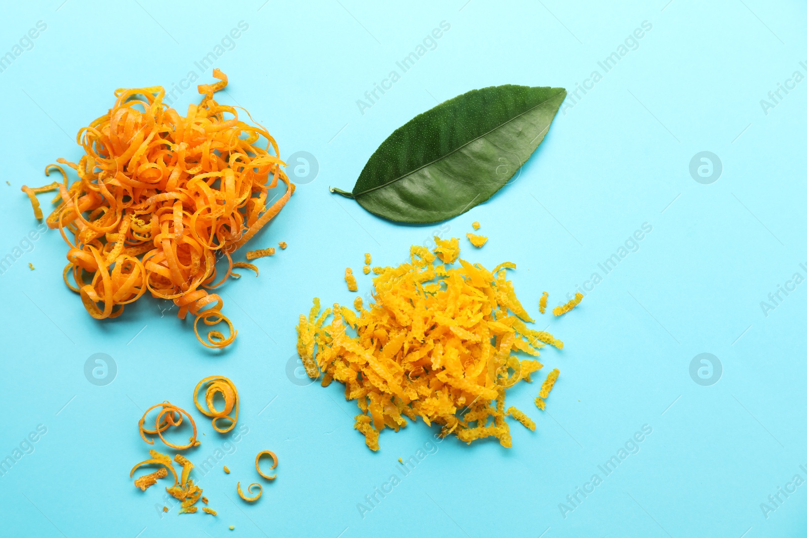 Photo of Flat lay composition with fresh orange zest and leaf on light blue background