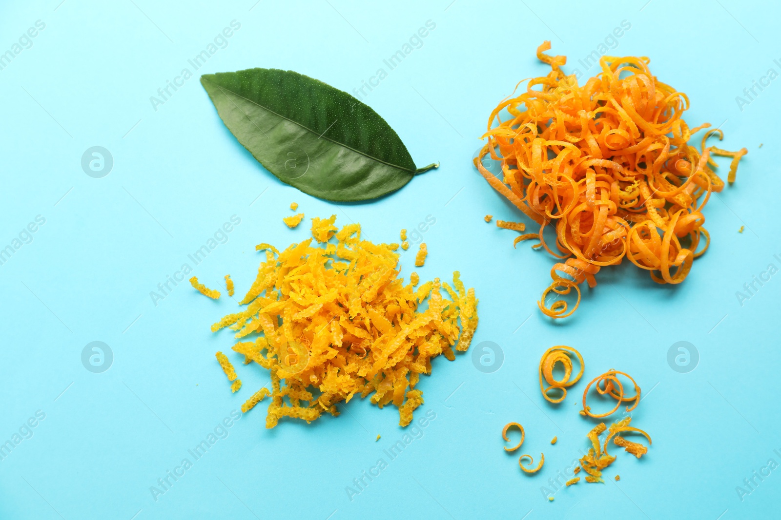 Photo of Flat lay composition with fresh orange zest and leaf on light blue background