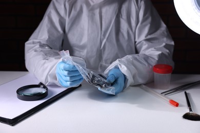 Photo of Forensic expert examining evidence in plastic bag at table indoors, closeup