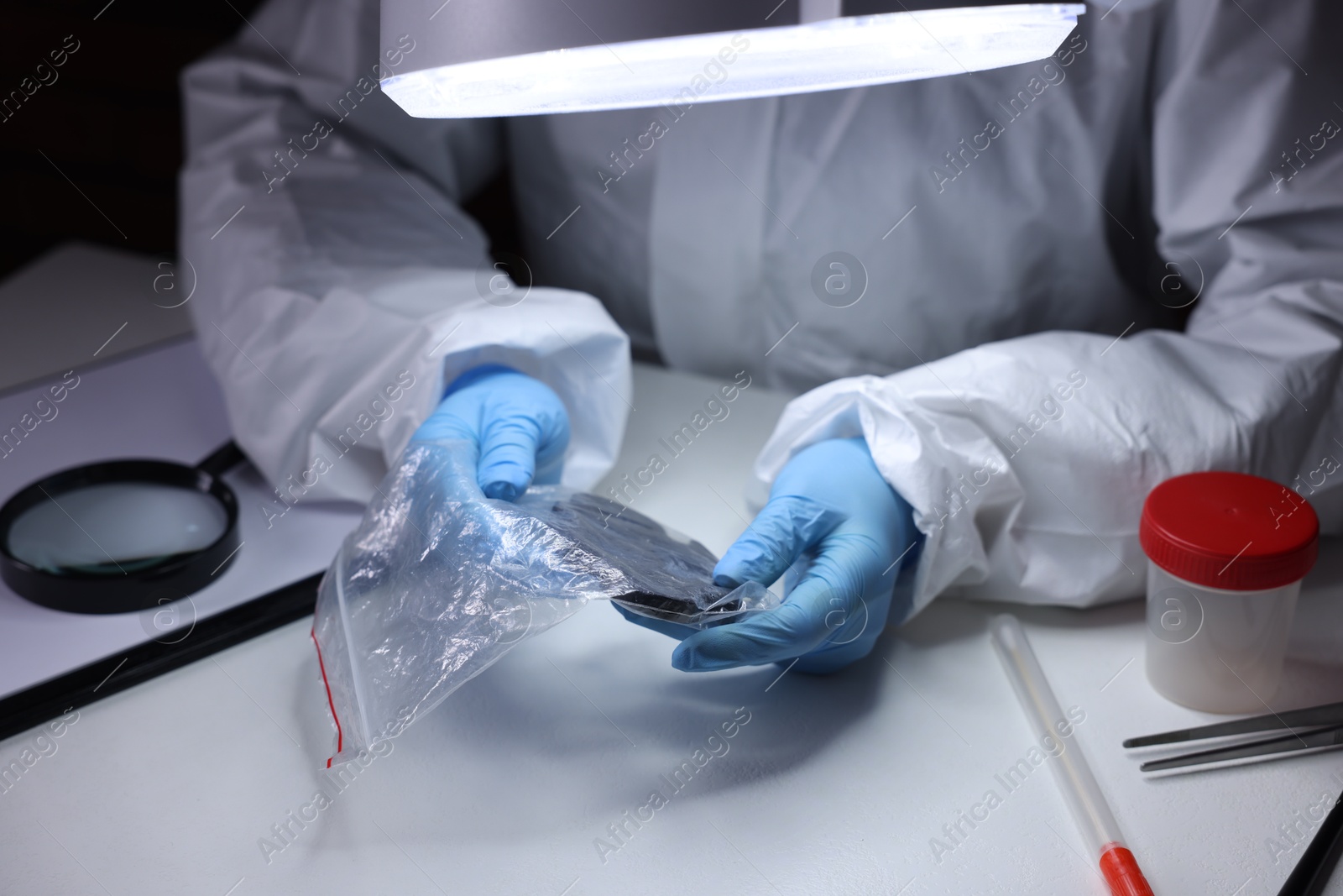 Photo of Forensic expert examining evidence in plastic bag at table indoors, closeup