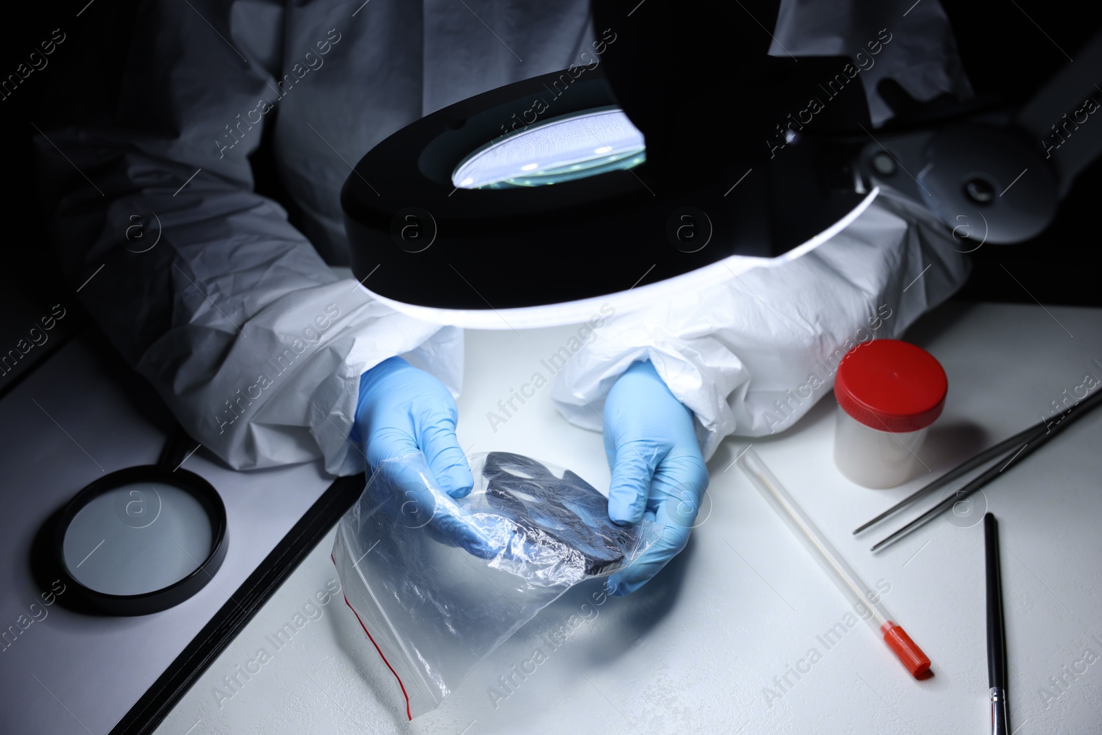 Photo of Forensic expert examining evidence in plastic bag at table indoors, closeup