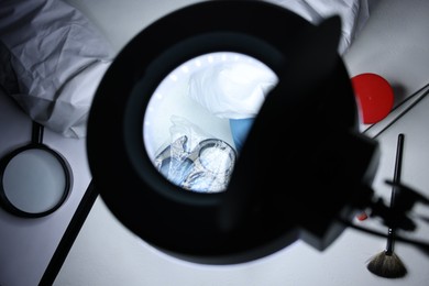 Photo of Forensic expert examining evidence in plastic bag at table indoors, top view