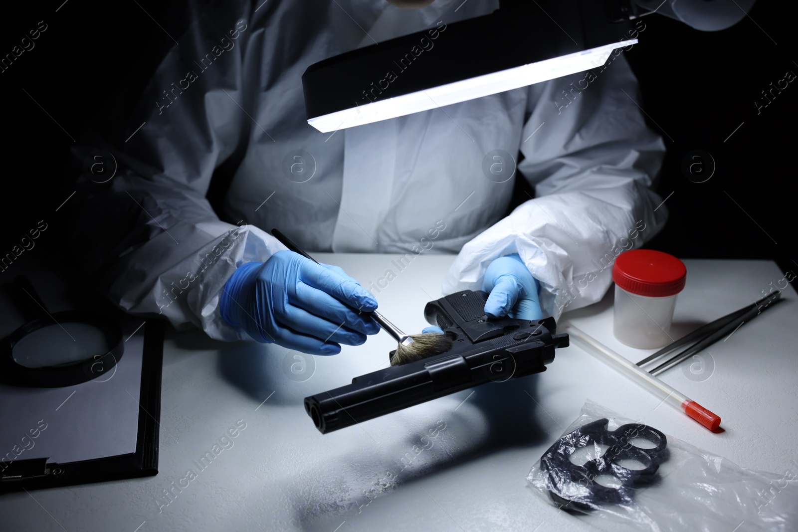 Photo of Forensic expert taking fingerprints with brush from gun at table indoors, closeup