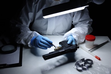 Photo of Forensic expert taking fingerprints with brush from gun at table indoors, closeup