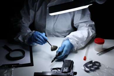 Photo of Forensic expert taking fingerprints with brush from knife at table indoors, closeup