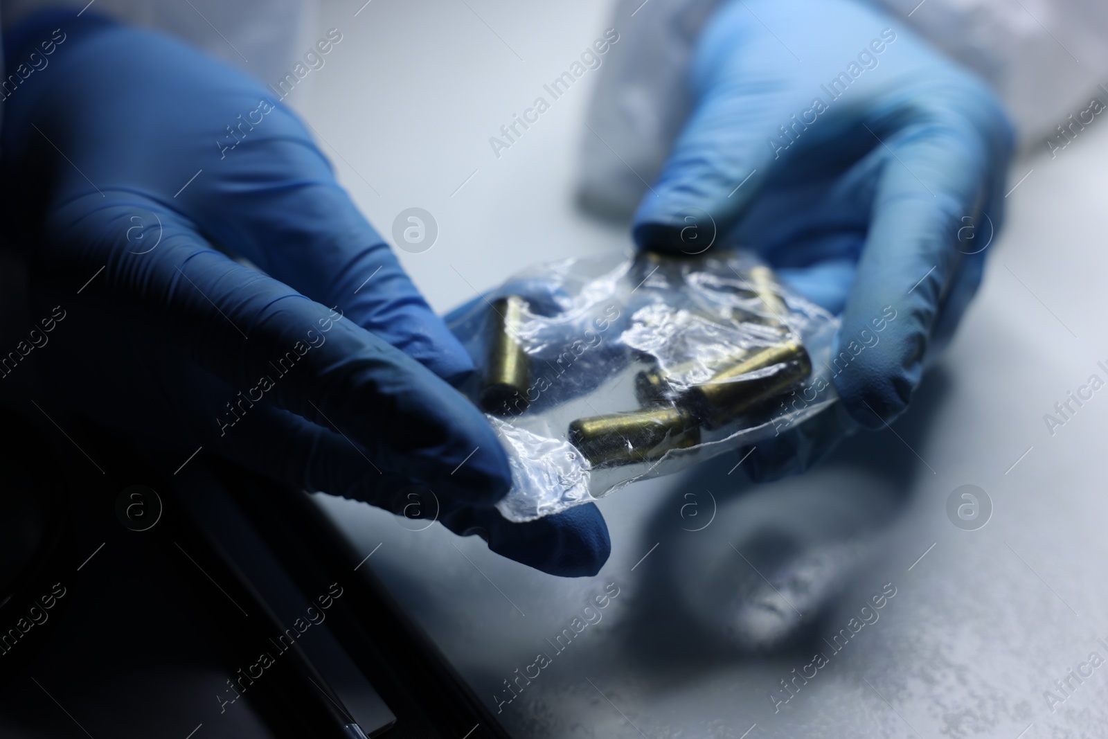 Photo of Forensic expert examining shell casings in plastic bag at table, closeup