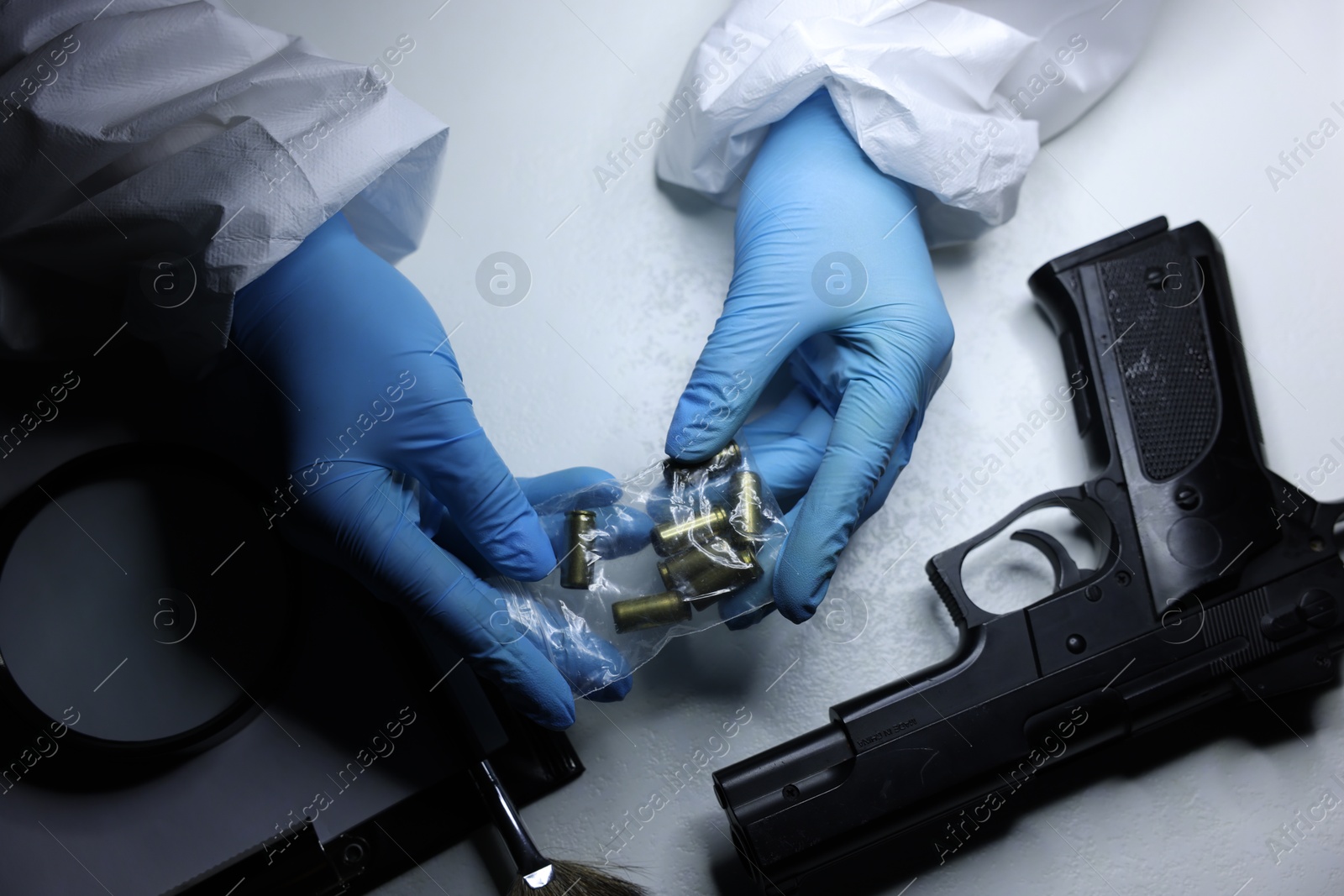 Photo of Forensic expert examining shell casings in plastic bag at table, top view