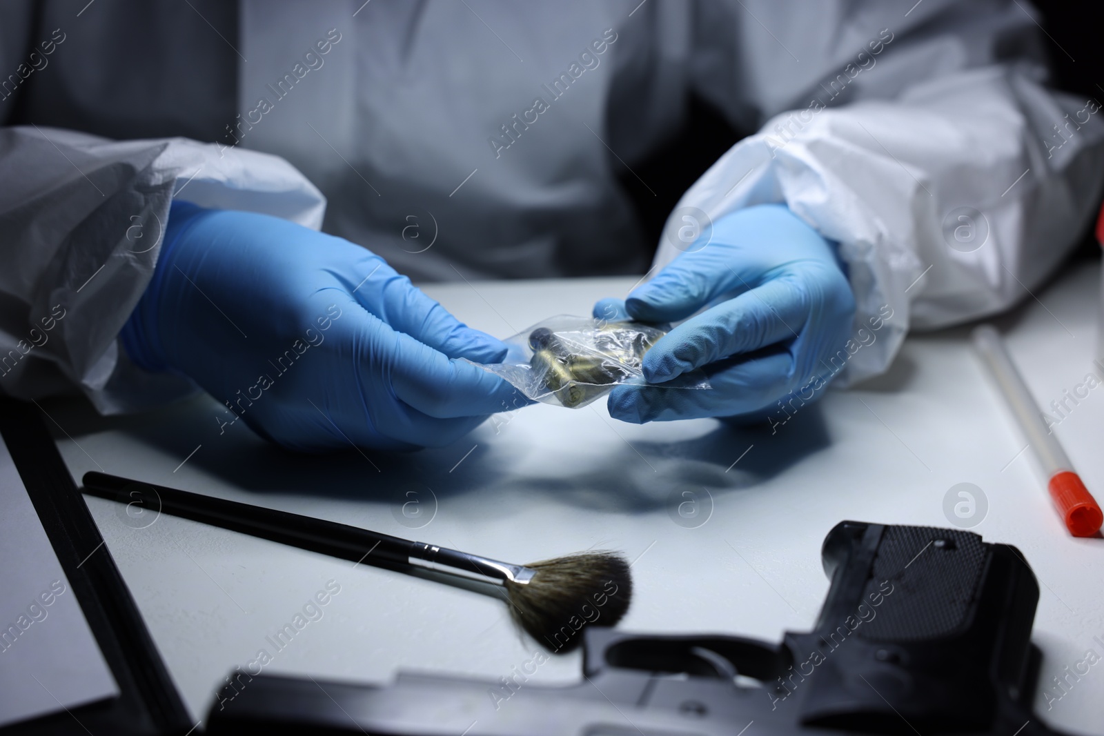 Photo of Forensic expert examining shell casings in plastic bag at table indoors, closeup