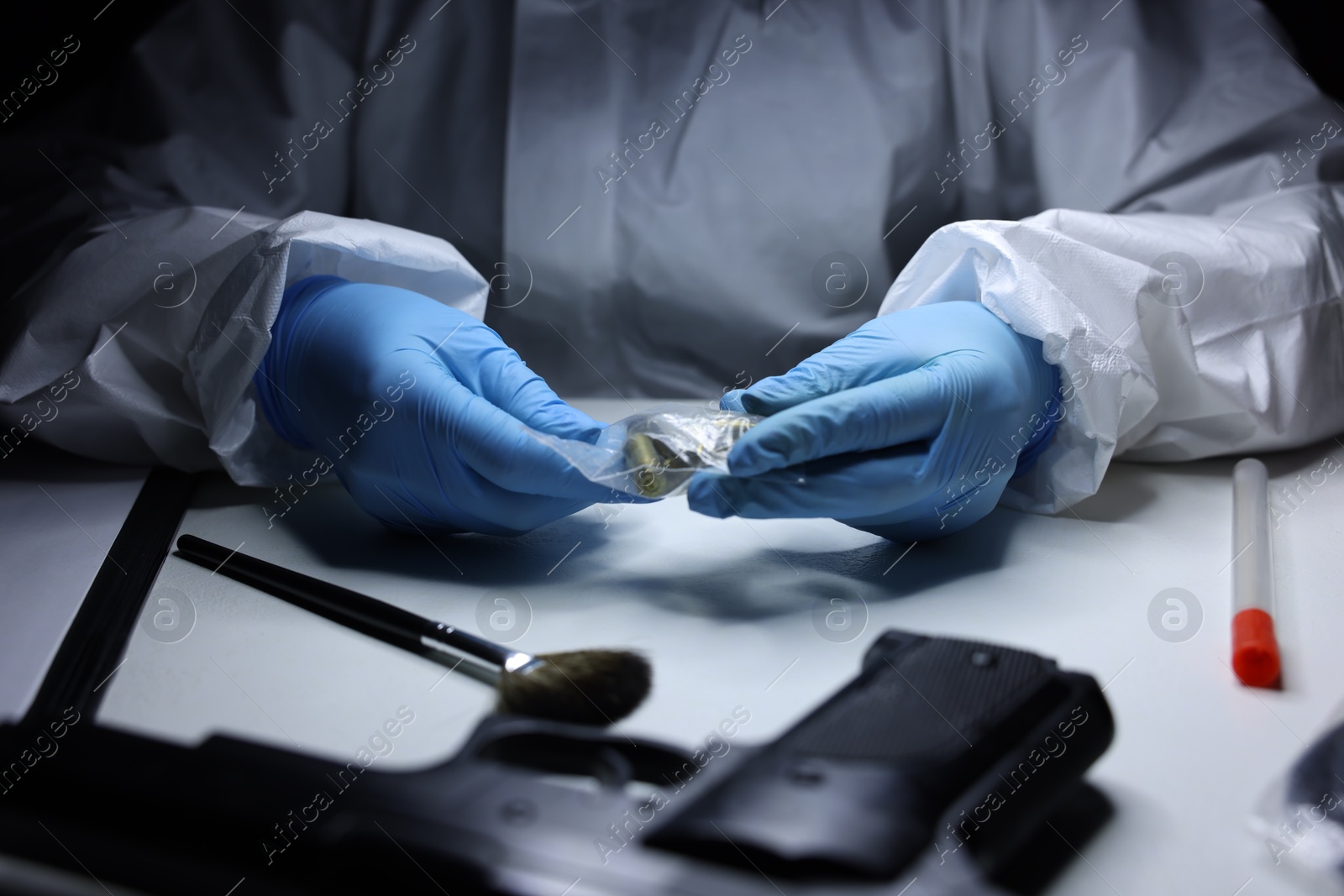 Photo of Forensic expert examining shell casings in plastic bag at table indoors, closeup