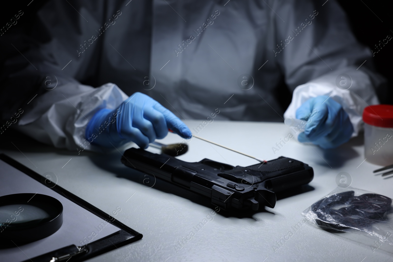 Photo of Forensic expert taking blood sample from gun at table indoors, closeup