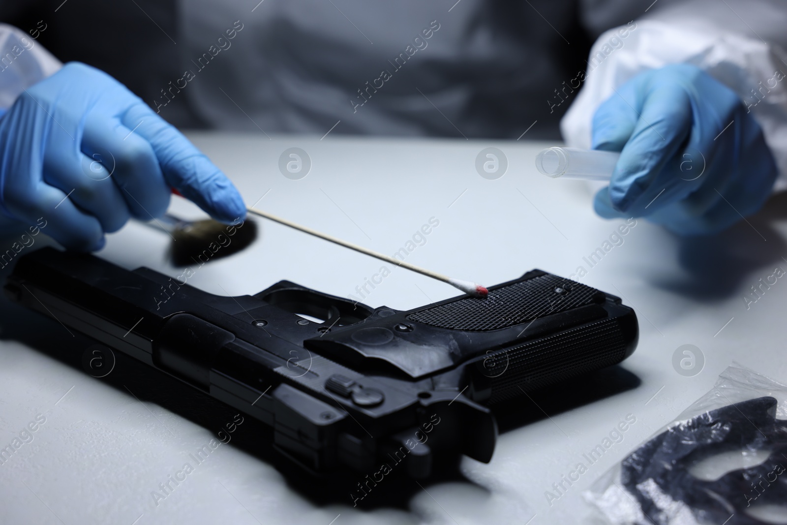 Photo of Forensic expert taking blood sample from gun at table indoors, closeup