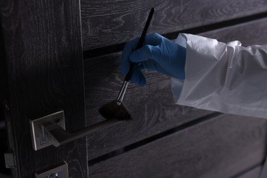 Photo of Forensic expert taking fingerprints with brush from handle of door, closeup