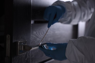 Photo of Forensic expert taking blood sample from handle of door, closeup