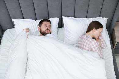 Resentful couple lying on bed at home, above view