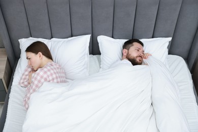 Resentful couple lying on bed at home, above view