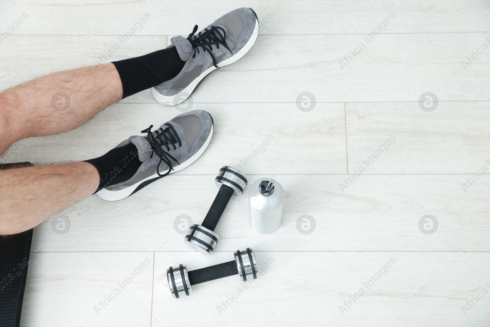 Photo of Man with thermo bottle and dumbbells on floor indoors, top view. Space for text