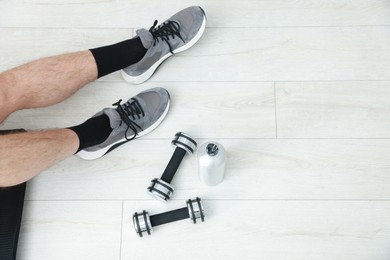 Photo of Man with thermo bottle and dumbbells on floor indoors, top view. Space for text