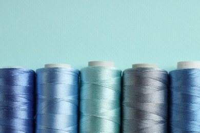 Photo of Different spools of sewing threads on light blue background, flat lay. Space for text