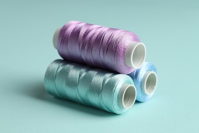 Photo of Different spools of sewing threads on light blue background, closeup