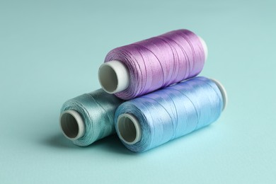 Photo of Different spools of sewing threads on light blue background, closeup