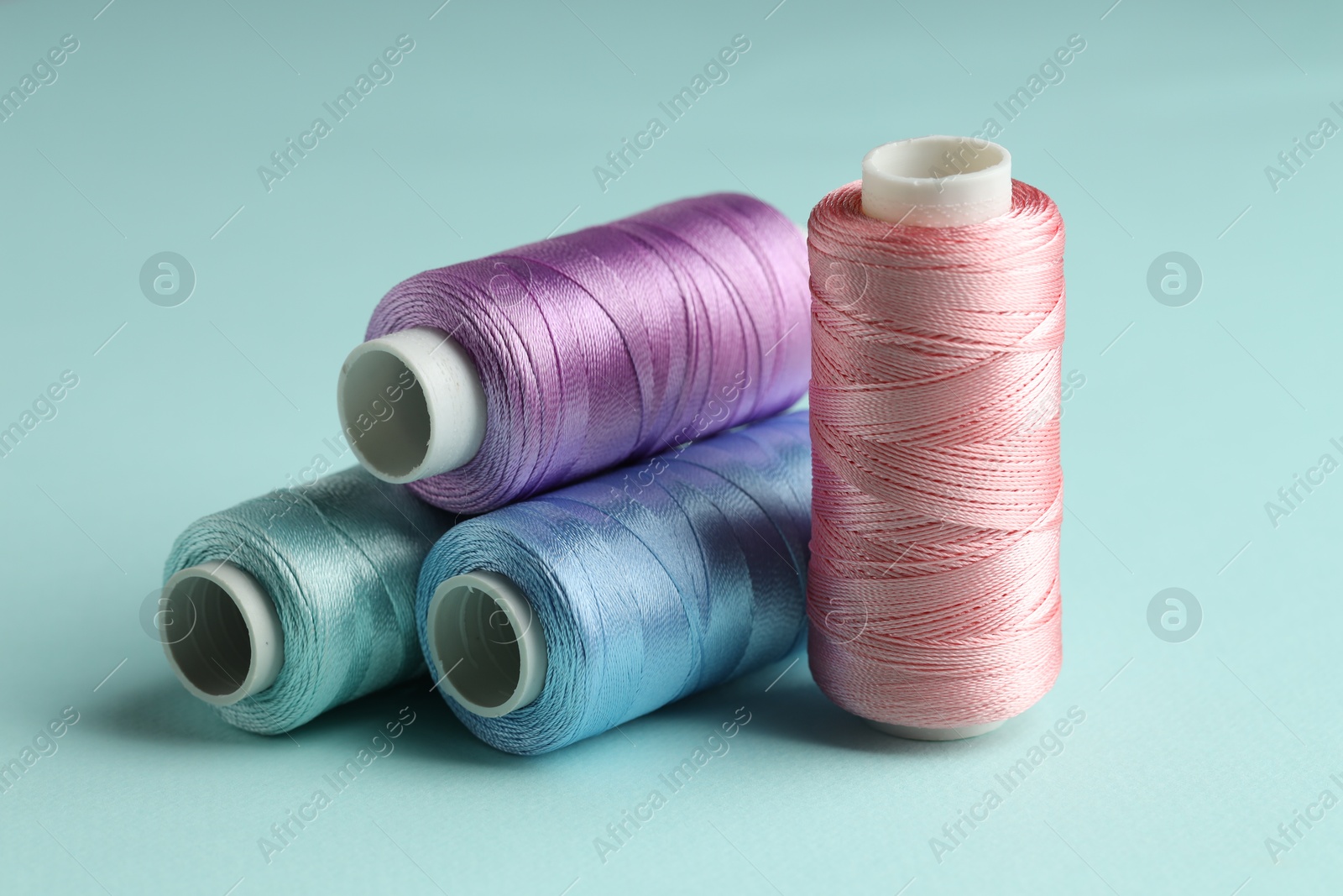 Photo of Different spools of sewing threads on light blue background, closeup