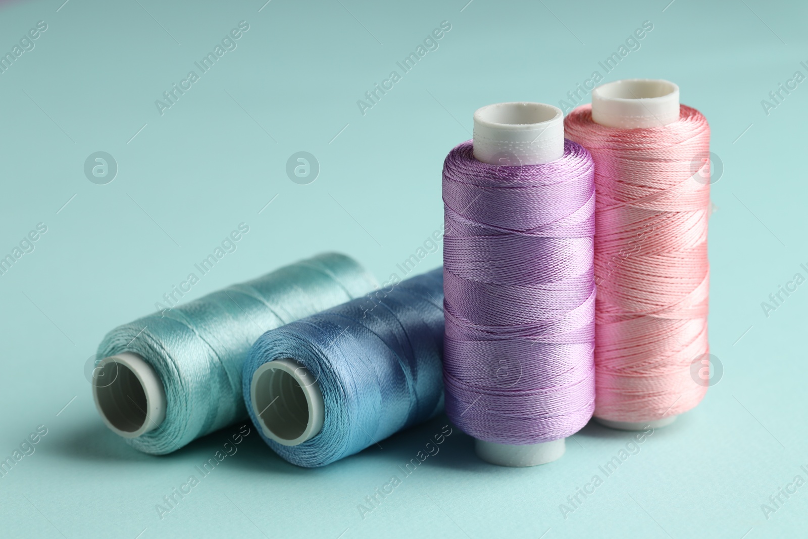 Photo of Different spools of sewing threads on light blue background, closeup