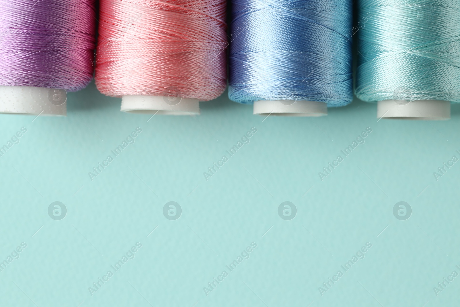 Photo of Different spools of sewing threads on light blue background, flat lay. Space for text