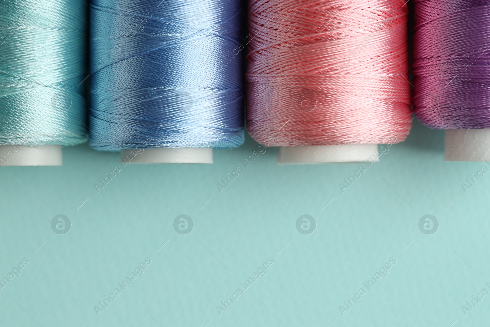 Photo of Different spools of sewing threads on light blue background, flat lay. Space for text