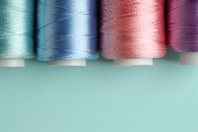 Photo of Different spools of sewing threads on light blue background, flat lay. Space for text