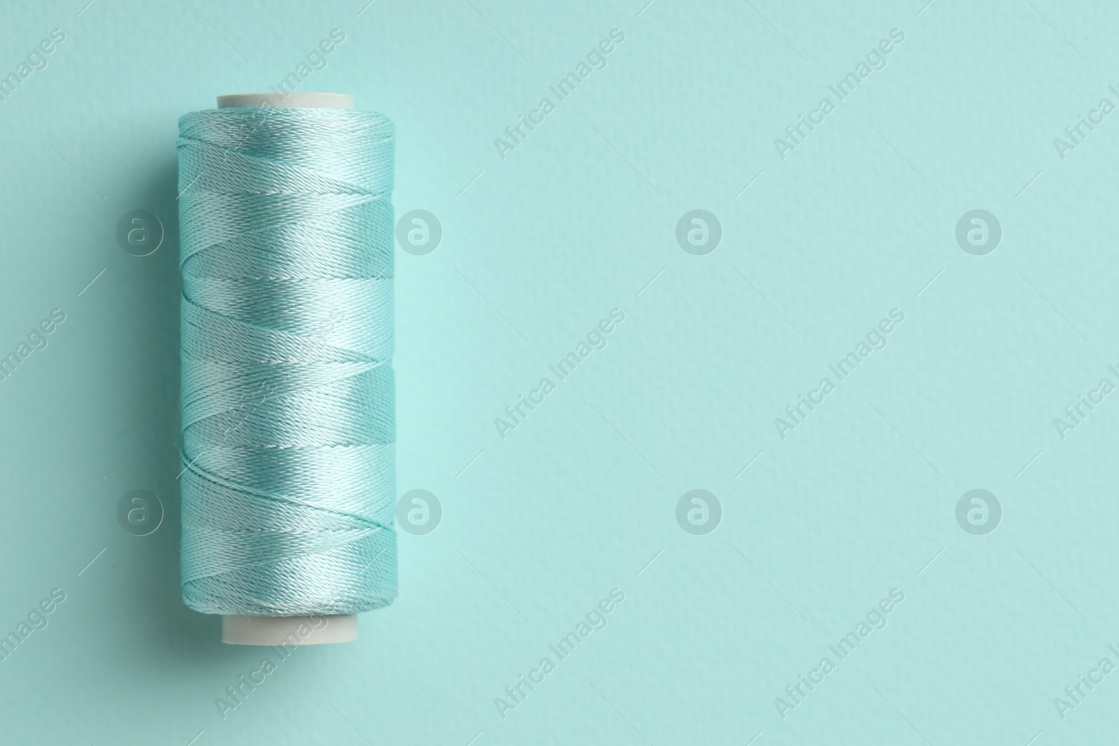 Photo of Spool of sewing thread on light blue background, top view. Space for text